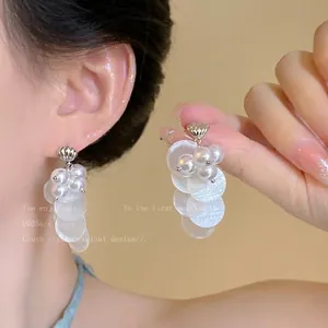 Détail de boucles d'oreilles pompons en nacre avec perles blanches et disques irisés