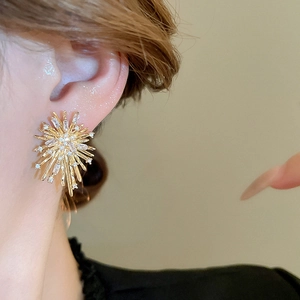 Close-up of golden sunburst firework earrings with sparkling cubic zirconia on model