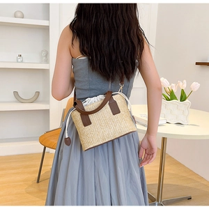 Detalle posterior de un bolso tipo cubo tejido en beige con correas de cuero marrón en modelo