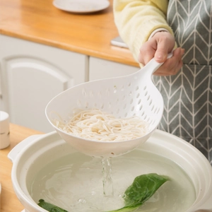 White nylon spider strainer spoon lifting noodles from a pot in a modern kitchen