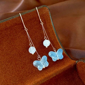 Détail de boucles d'oreilles papillon à pompons avec perles et breloques bleues
