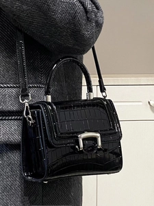 Detail view of glossy black crocodile pattern patent leather handbag with silver buckle