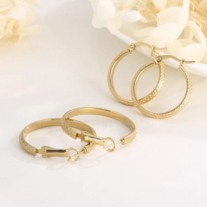 Textured gold-plated stainless steel hoop earrings with diamond pattern on white surface