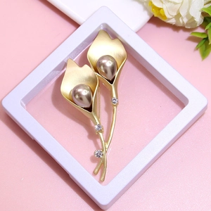 Close-up of golden calla lily brooch with pearls and rhinestones on pink background