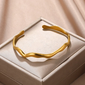Detail of a wavy gold open bangle with a matte finish displayed in a luxury jewelry box