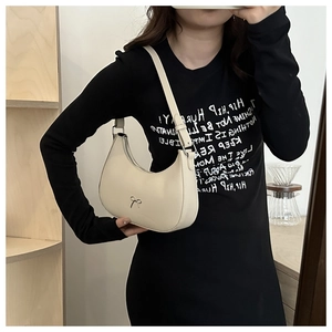 Minimalist beige crescent underarm bag with metal bow detail shown in lifestyle setting