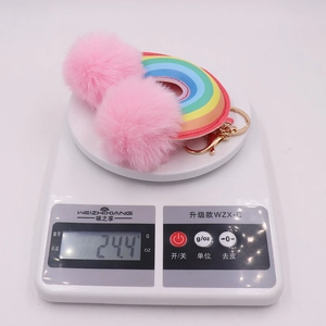 Rainbow faux leather keychain with two pink plush pom poms being weighed on digital scale