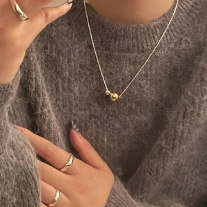 Close-up of dual-tone bead pendant necklace and silver rings on a grey sweater