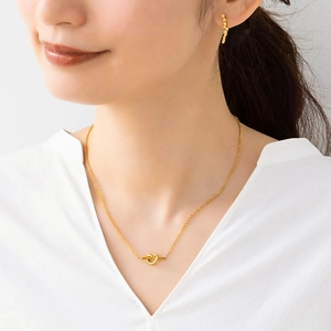 Close-up of golden knotted heart pendant necklace and matching earrings worn by a model
