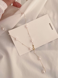 Close-up of elegant pearl necklace with gold chain on white fabric background