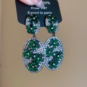 Close-up of vintage oval drop earrings with emerald flowers and paved white zircons
