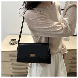 Elegant black matte leather shoulder bag with a gold metal buckle worn in a minimalist interior
