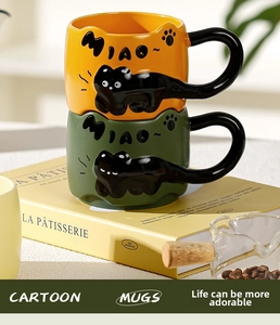 Close-up of 3D relief black cat ceramic mugs in yellow and green with 'MIAO' text