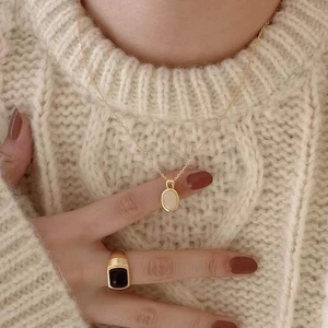 Close-up of elegant gold necklace with shell pendant and black stone ring on model