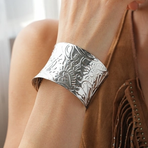 Detailed macro view of the silver embossed floral patterns on the wide metal cuff bracelet