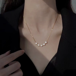 Minimalist gold titanium necklace with five white pearls worn on a female neck