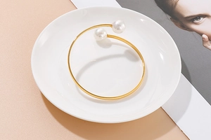 Detailed view of an open golden bangle with two white pearls on a ceramic dish