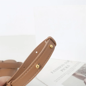 Gros plan sur la bandoulière en cuir marron avec rivets dorés et coutures précises