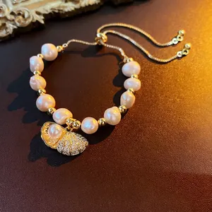 Elegant freshwater pearl shell bracelet with adjustable gold chain on leather surface