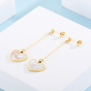 Detail of gold dangle earrings with mother of pearl heart pendants on white display
