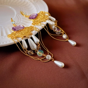 Close-up of vintage palace style earrings with purple gems, pearls, and gold tassels