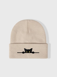 Dettaglio ravvicinato di un berretto beige in maglia con ricamo a forma di gatto nero