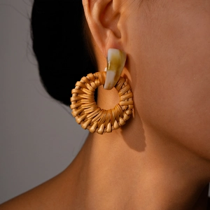 Close-up of bohemian style woven resin earrings worn by a model in warm lighting