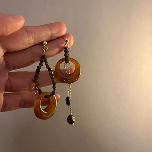Detail of asymmetric tiger eye resin earrings with gold accents held by hand