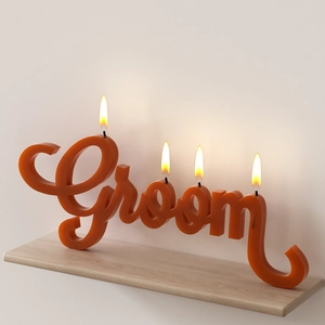 Close-up of Groom word art candle in orange-red wax with four burning wicks on wood