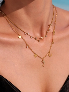 Detail of layered gold-tone necklace featuring zircon dolphin and clover charms on model