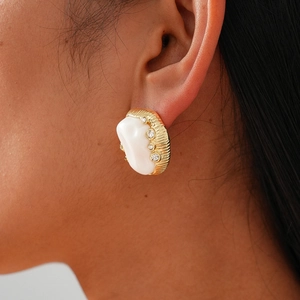 Close-up of golden oval earring with textured edge and white resin on female model