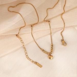 Elegante goldene Edelstahl-Herzkette mit Perlen auf beigem Samthintergrund für Damen