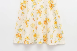 Detail von gelbem Blumendruckstoff mit Rosenmustern auf einem weißen Sommerkleid