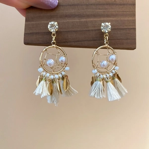 Close-up of dreamcatcher tassel earrings with pearls and gold leaf accents