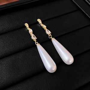 Eleganti orecchini dorati con zirconi e grandi perle a goccia bianche su sfondo nero
