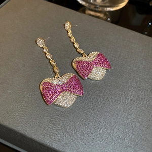 Detailed close-up of bow and heart earrings with pink rhinestones and gold chains