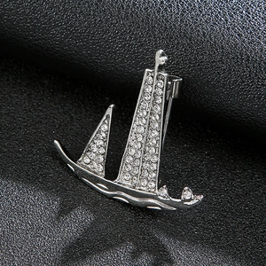 Macro shot of silver sailboat brooch with crystal rhinestones on black leather texture