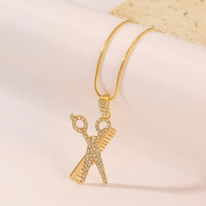 Close-up of golden scissors and comb pendant with pavé crystals on white silk