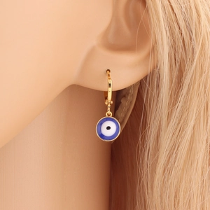 Close-up of a gold hoop earring with a blue enamel evil eye pendant worn by a model