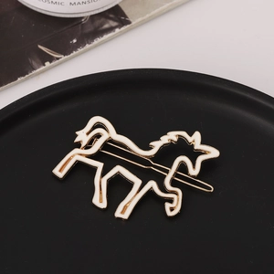 Macro detail of gold unicorn hair clip with white enamel finish on matte black tray
