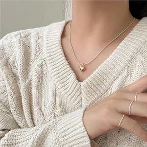 Minimalist gold heart pendant necklace and beaded rings on a model in cream sweater