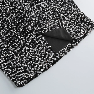 Detailed close-up of silver sequins on black fabric dress with split hem and lining