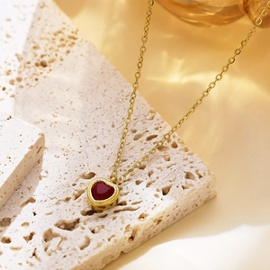 Macro shot of 18k gold heart pendant necklace with red zircon on travertine stone