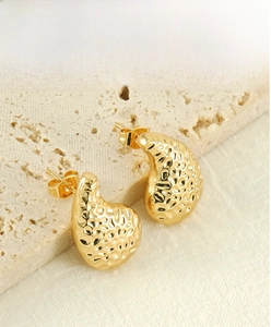 Vue macro de boucles d'oreilles goutte dorées avec texture martelée sur une surface en pierre