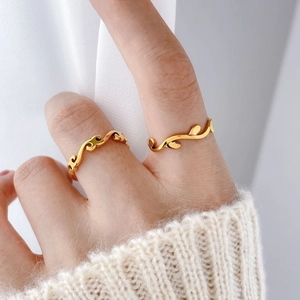 Detail shot of gold wave and vine leaf rings on finger with cozy knit background