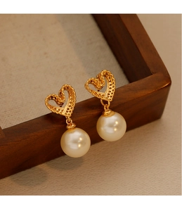 Macro shot of gold hollow heart earrings with elegant white pearl drops on wood