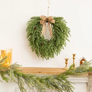 Couronne de Noël en forme de cœur avec aiguilles de pin et nœud en toile sur mur blanc