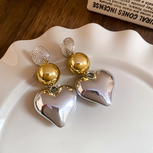 Close-up of mixed metal heart drop earrings featuring silver textured studs and gold spheres