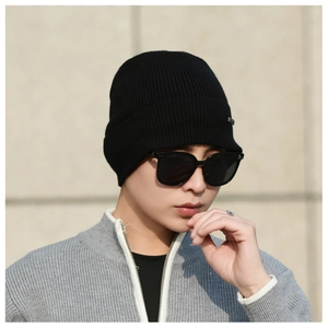 Detailed texture of black ribbed knit beanie featuring a small metal decorative logo accent