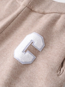 Detailed close-up of light brown knitted fabric featuring a white boucle letter C patch